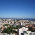 Vista panorâmica de Lisboa, com edifícios da cidade e o rio Tejo ao fundo.