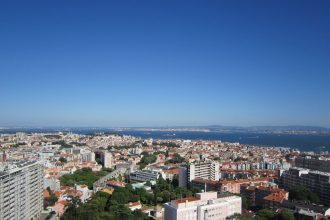 Vista panorâmica de Lisboa, com edifícios da cidade e o rio Tejo ao fundo.