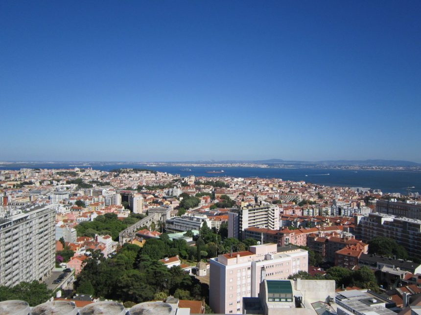 Vista panorâmica de Lisboa, com edifícios da cidade e o rio Tejo ao fundo.