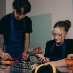 Dois jovens trabalham em um projeto de eletrônica em um laboratório, analisando componentes e circuitos.