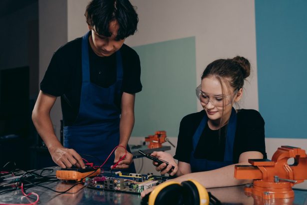 Dois jovens trabalham em um projeto de eletrônica em um laboratório, analisando componentes e circuitos.