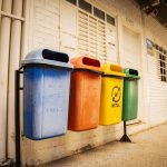 Quatro contentores para separação de papel, plástico, metal e vidro num espaço interior.
