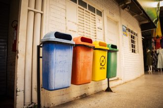 Quatro contentores para separação de papel, plástico, metal e vidro num espaço interior.
