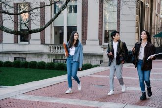 Grupo de estudantes caminha por um passeio de um campus universitário num dia de sol.