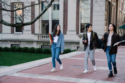 Grupo de estudantes caminha por um passeio de um campus universitário num dia de sol.