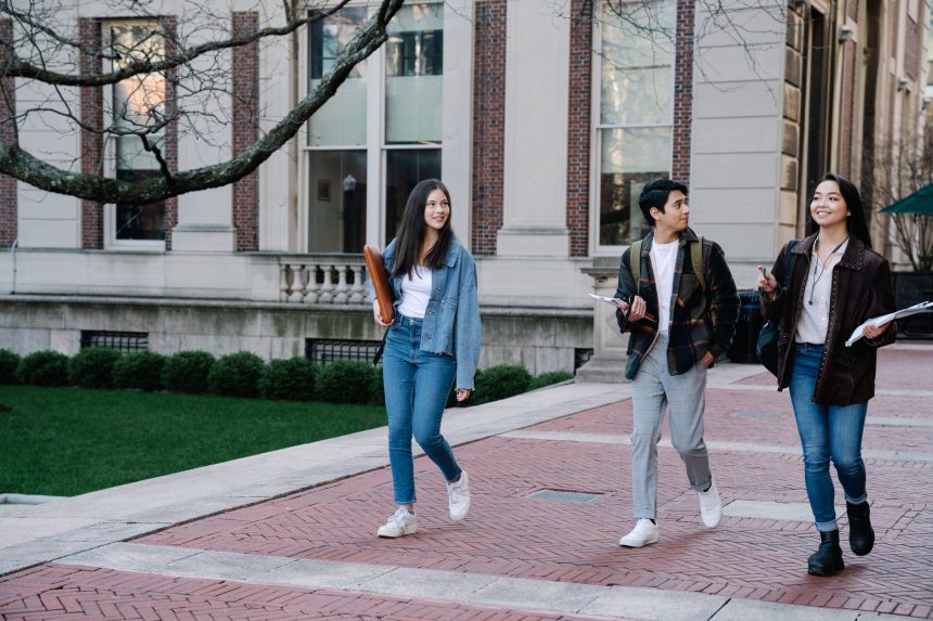 Grupo de estudantes caminha por um passeio de um campus universitário num dia de sol.
