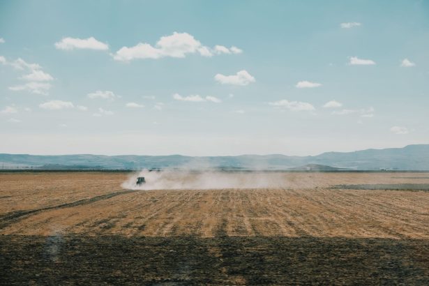Trator levanta poeira enquanto trabalha num extenso campo agrícola sob céu limpo.