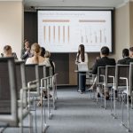 Participantes de uma conferência acompanham uma apresentação com gráficos sobre dados econômicos.