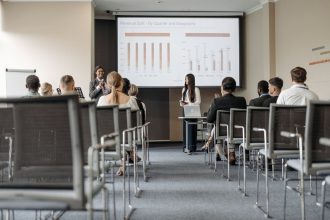Participantes de uma conferência acompanham uma apresentação com gráficos sobre dados econômicos.