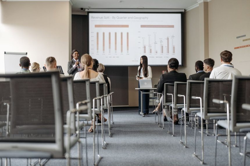 Participantes de uma conferência acompanham uma apresentação com gráficos sobre dados econômicos.