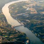 Vista aérea da barragem de Crestuma, no rio Douro, rodeada por paisagem verdejante.
