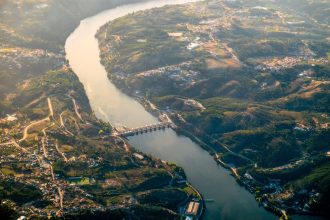 Vista aérea da barragem de Crestuma, no rio Douro, rodeada por paisagem verdejante.