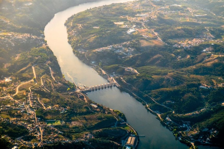 Vista aérea da barragem de Crestuma, no rio Douro, rodeada por paisagem verdejante.