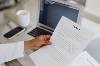 Pessoa segura um documento contratual junto a um computador portátil durante uma sessão de trabalho.