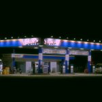 Posto de combustíveis iluminado à noite, com caminhões e carros estacionados.