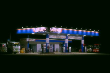 Posto de combustíveis iluminado à noite, com caminhões e carros estacionados.