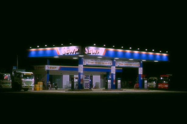 Posto de combustíveis iluminado à noite, com caminhões e carros estacionados.