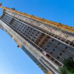 Gruas de construção sobre um edifício em obra, com a silhueta da cidade ao fundo, ilustrando o setor da habitação.